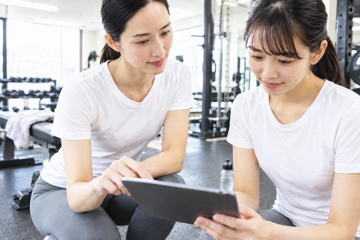 座った利用者の横にかがみ、タブレットの画面を一緒に見るトレーナー