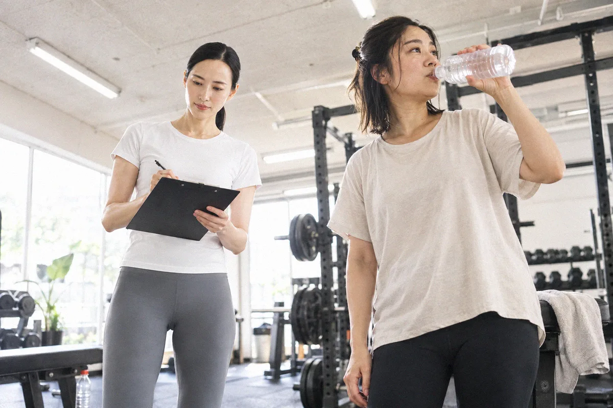 セットの合間に水分を取る利用者と、次の種目を確認するトレーナー