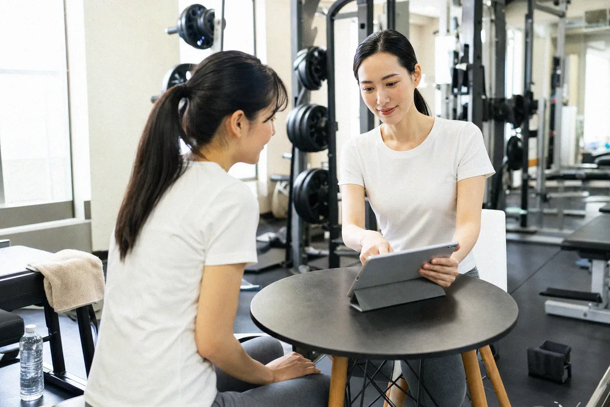 丸テーブルでタブレットを見せながら話すトレーナーと利用者