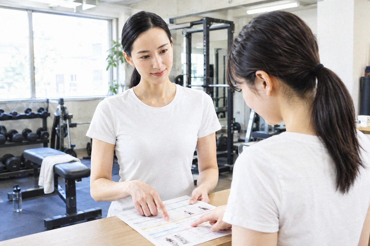 受付カウンターで印刷したプランを指しながら確認する利用者とトレーナー