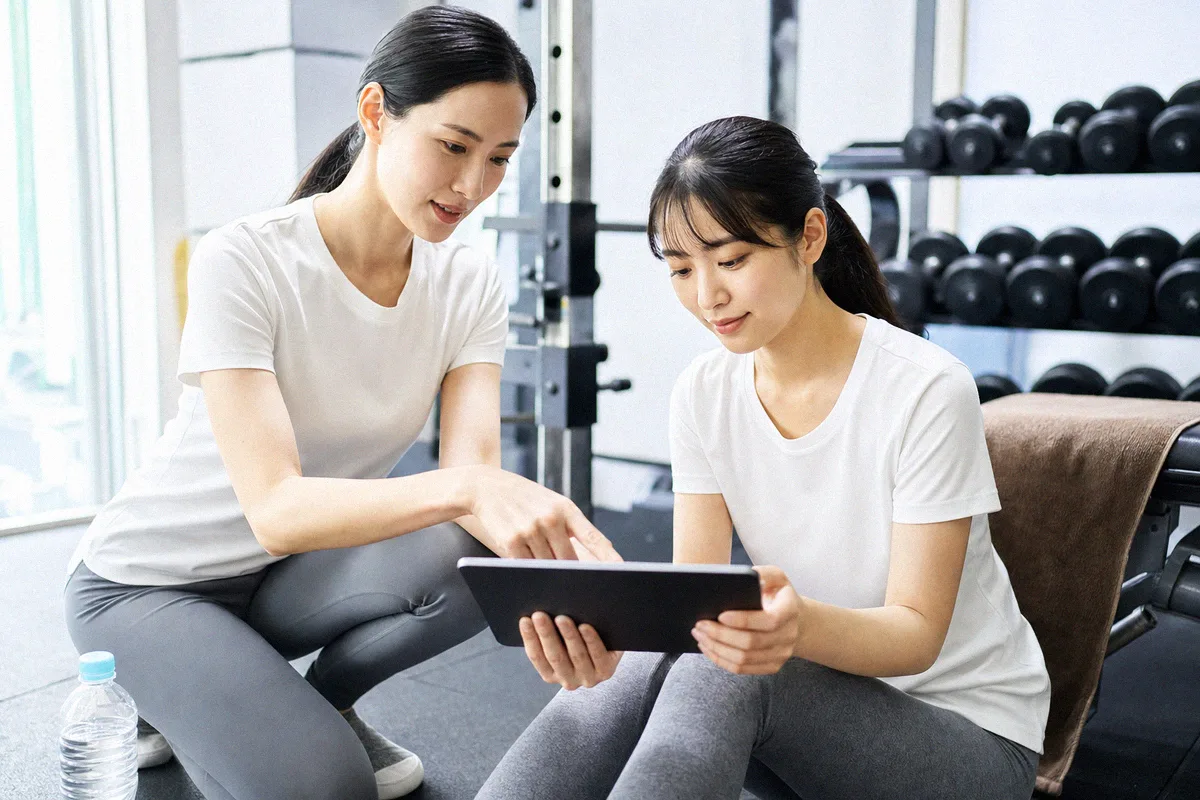 利用者の横に腰かけ、タブレットを指しながら説明するトレーナー
