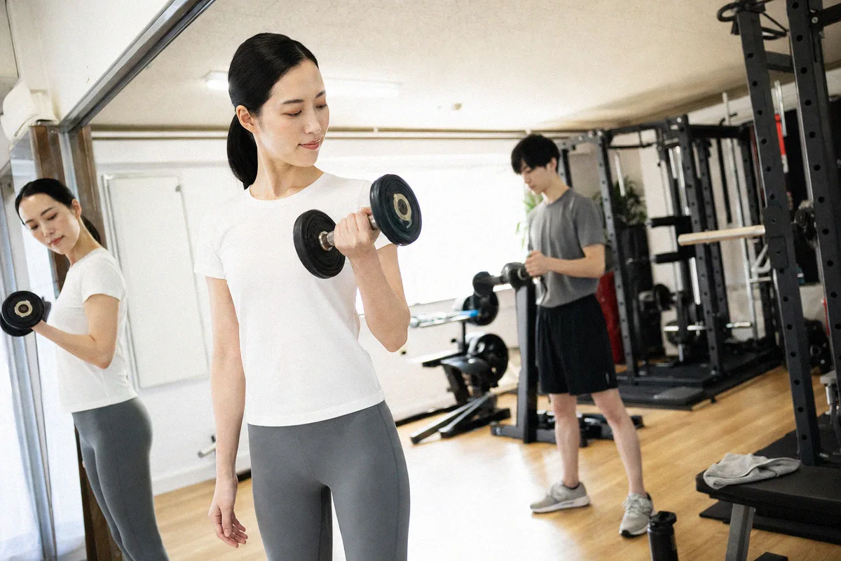 スタジオで黙々とダンベルを持ち上げる利用者、奥にトレーナー