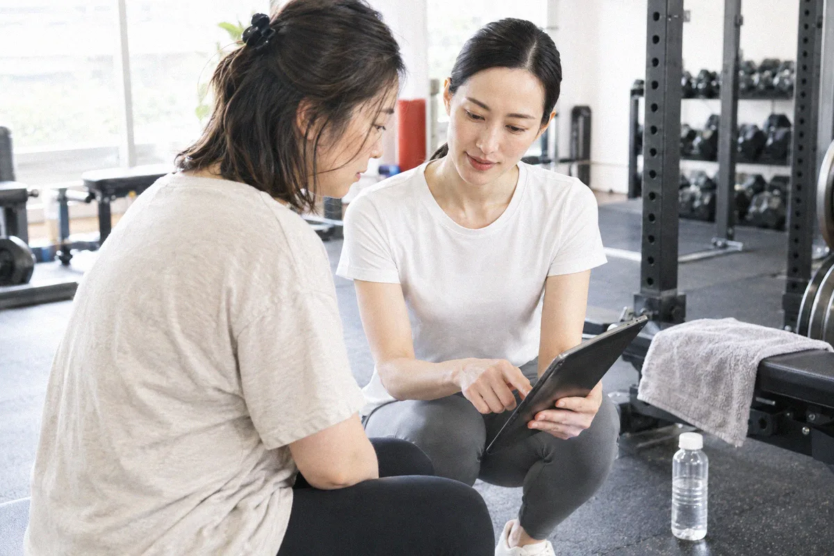 座った利用者の横にかがみ、タブレットの画面を一緒に見るトレーナー