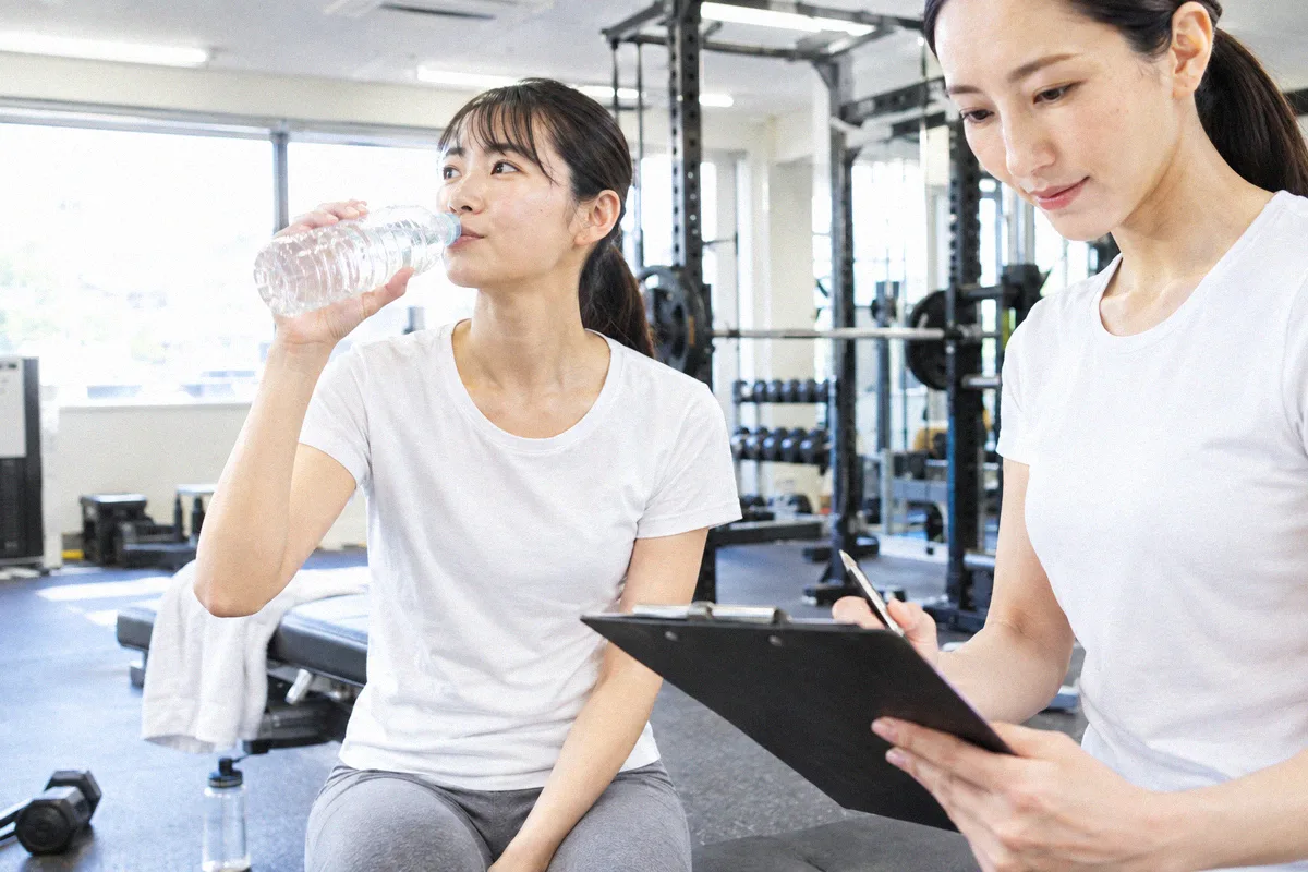 セットの合間に水分を取る利用者と、次の種目を確認するトレーナー