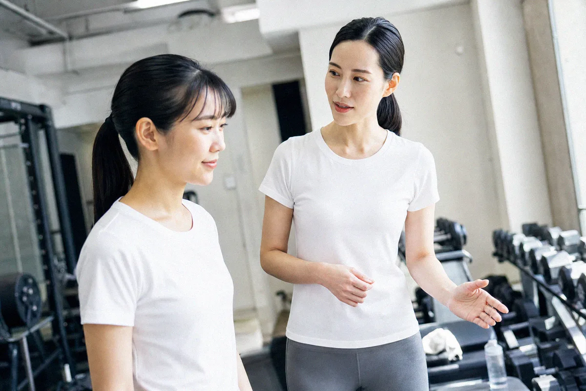 トレーニング機材が並ぶスタジオで並んで立つトレーナーと利用者