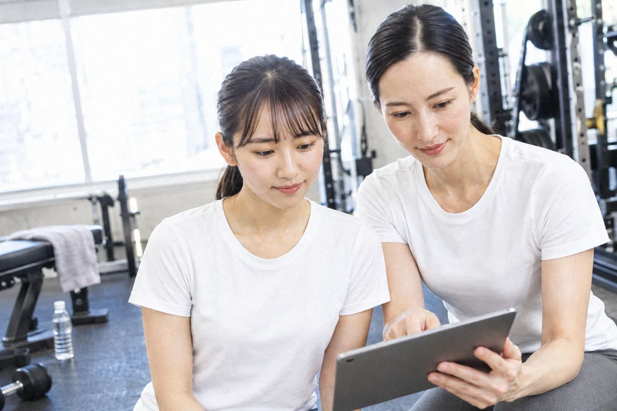 座った利用者の横にかがみ、タブレットの画面を一緒に見るトレーナー