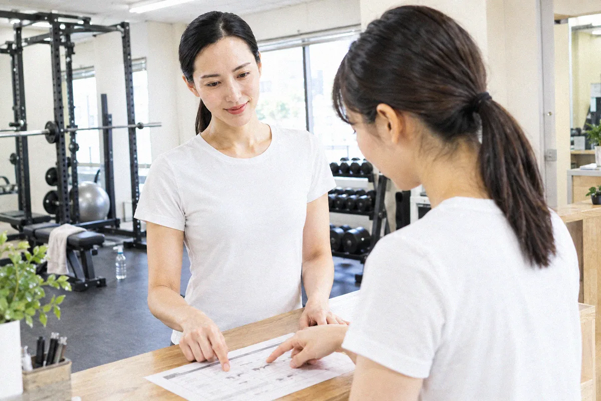 受付カウンターで印刷したプランを指しながら確認する利用者とトレーナー