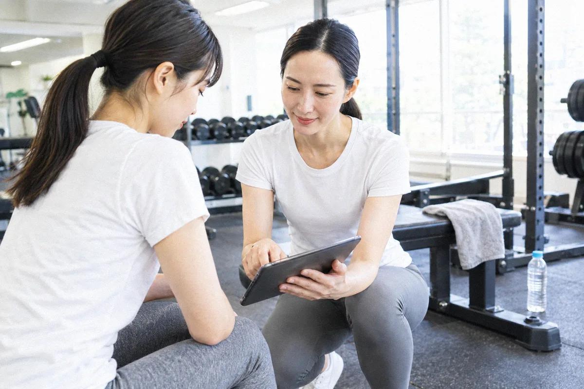 座った利用者の横にかがみ、タブレットの画面を一緒に見るトレーナー