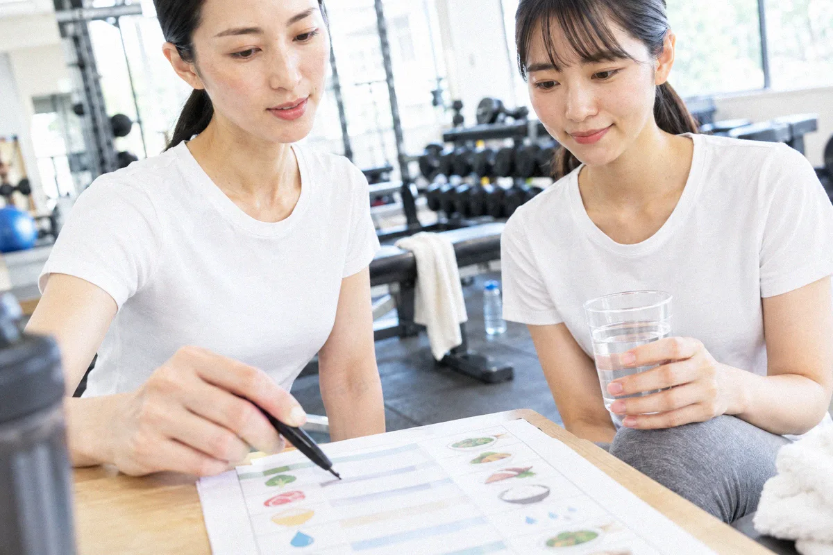 栄養バランス表を指しながら説明するトレーナーと、水を持つ利用者