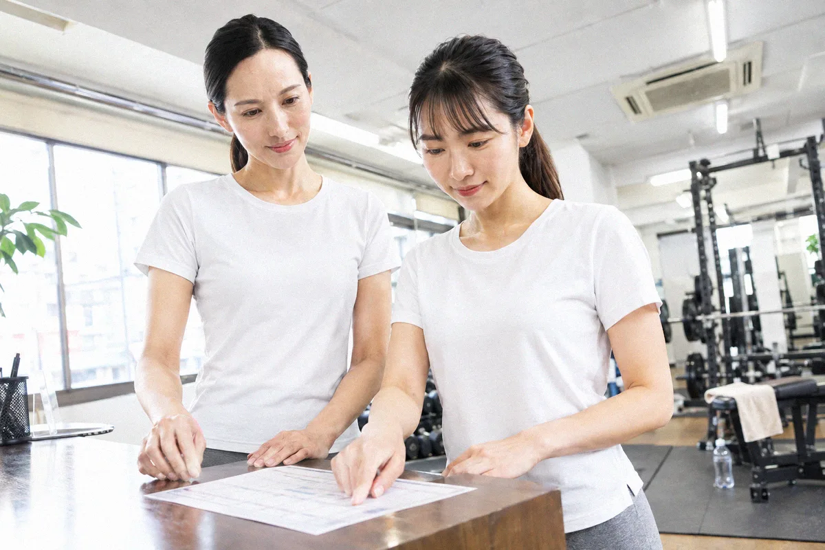 受付カウンターで印刷したプランを指しながら確認する利用者とトレーナー
