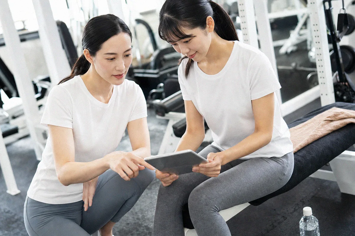 ベンチに並んで座り、タブレットで計画を確認するトレーナーと利用者