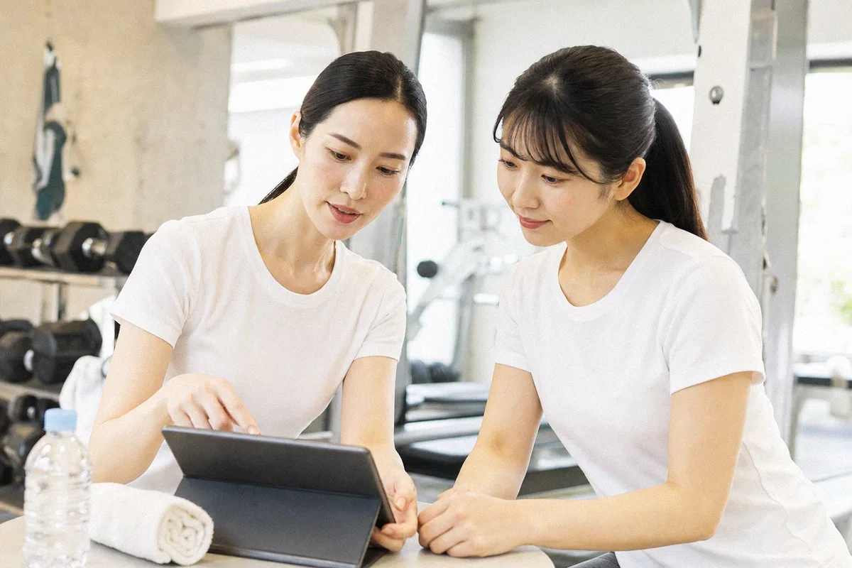 テーブルに置いたタブレットを指しながら説明するトレーナーと利用者