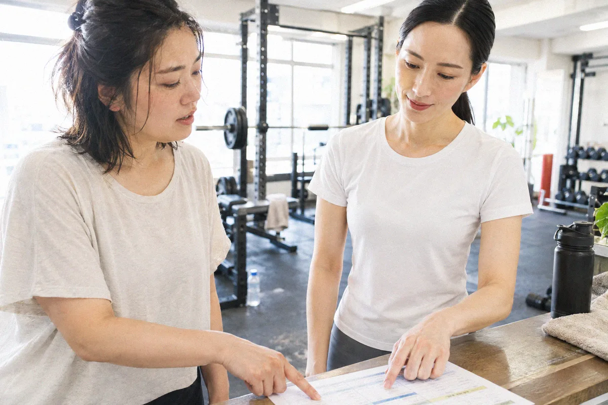 受付カウンターで印刷したプランを指しながら確認する利用者とトレーナー