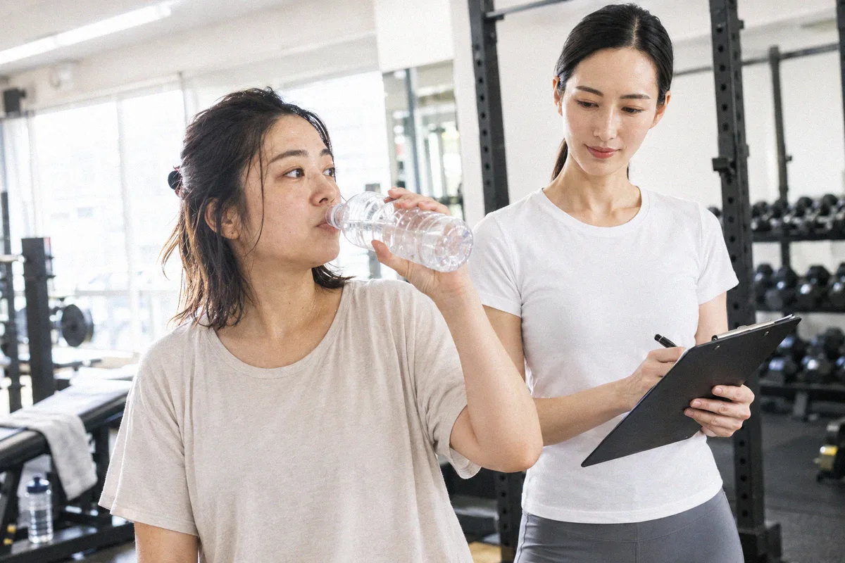 セットの合間に水分を取る利用者と、次の種目を確認するトレーナー