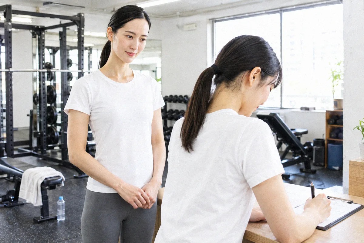 初回の申込用紙に記入する利用者と、横で待つトレーナー