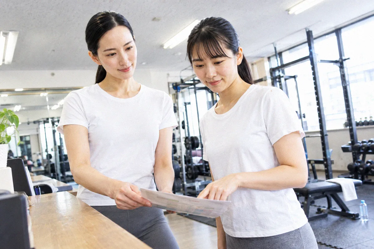 受付カウンターで印刷したプランを指しながら確認する利用者とトレーナー