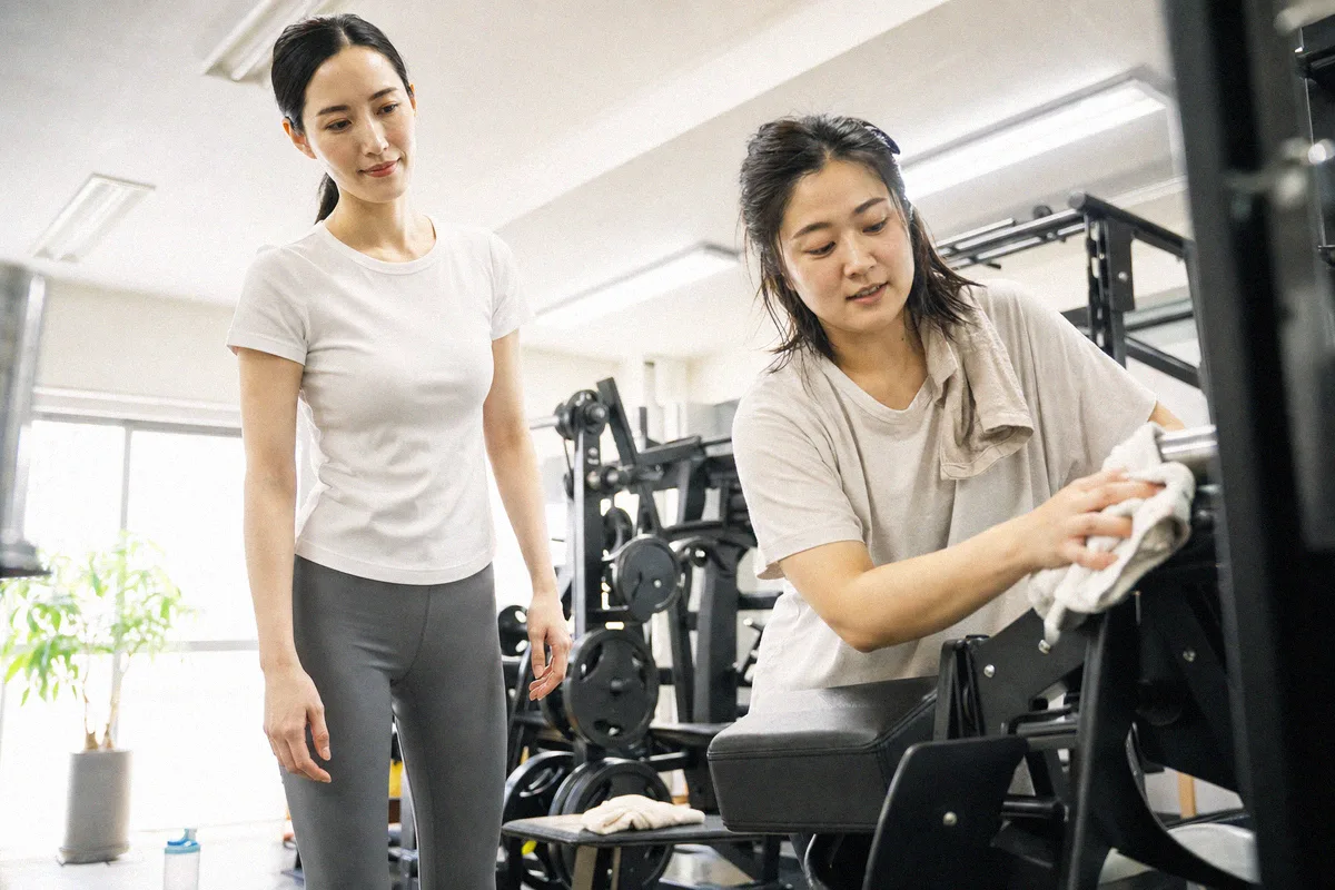 スタジオで黙々とダンベルを持ち上げる利用者、奥にトレーナー