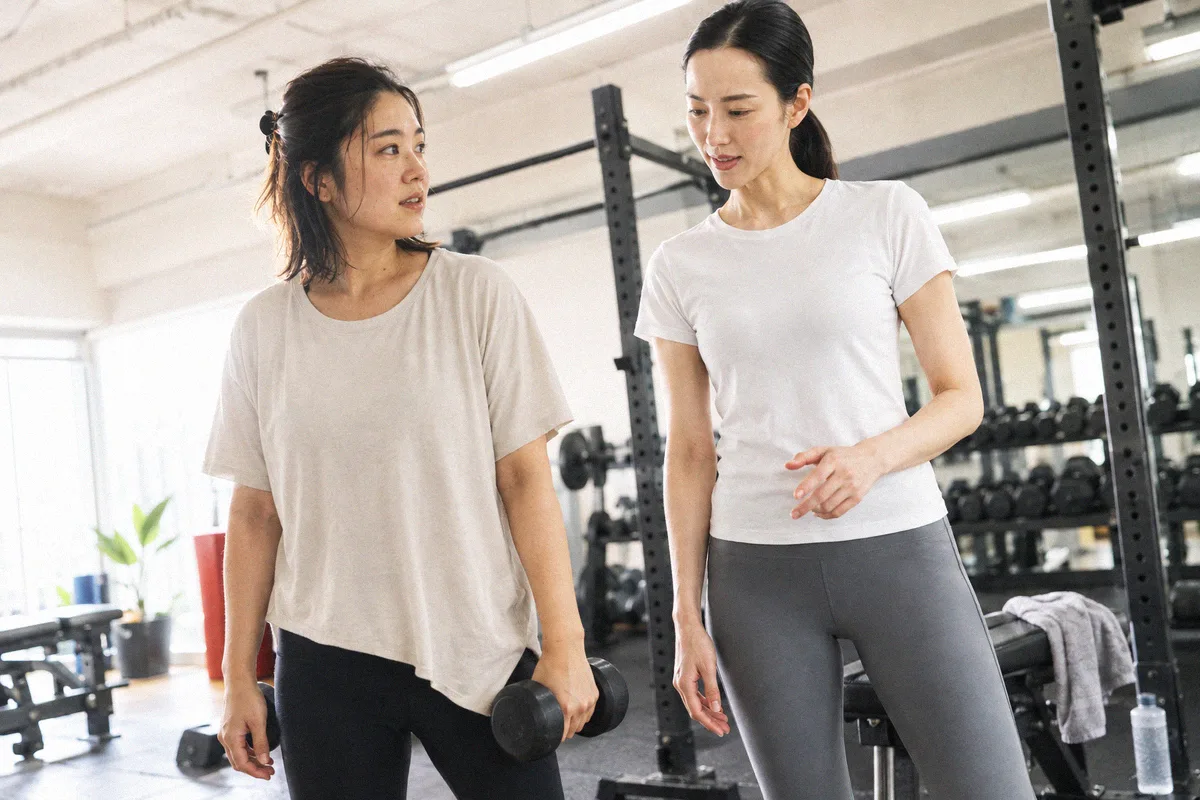 ダンベルを手にトレーナーと話しながらフロアを歩く利用者