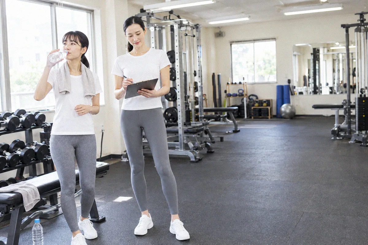 セットの合間に水分を取る利用者と、次の種目を確認するトレーナー