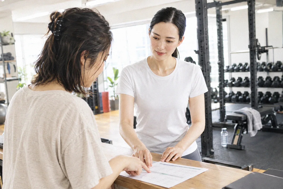 受付カウンターで印刷したプランを指しながら確認する利用者とトレーナー