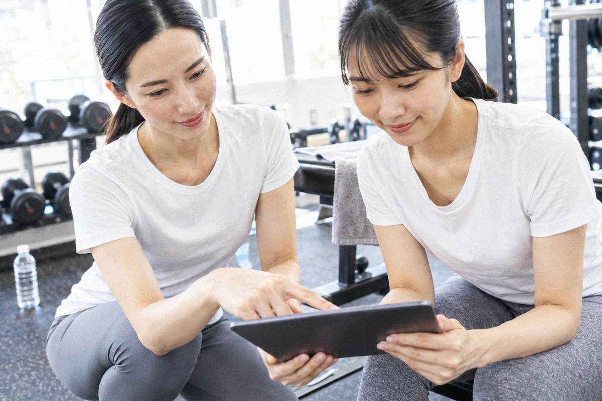 座った利用者の横にかがみ、タブレットの画面を一緒に見るトレーナー